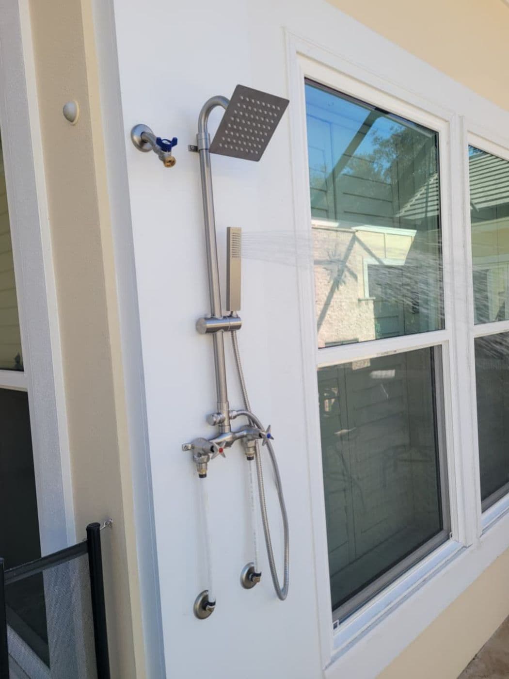 Stainless steel outdoor shower mounted beside a window